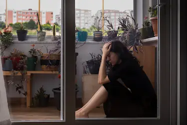 Femme effondrée sur le rebord d'une fenêtre, tête dans les mains, illustrant l'épuisement du burn-out