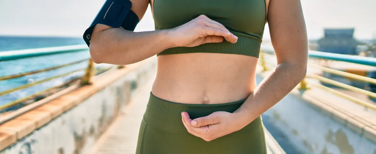 Femme sportive les mains sur le ventre en plein air, évoquant la santé intestinale et le microbiote en naturopathie