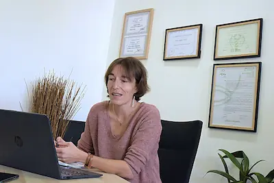 Agnès Guet naturopathe concentrée sur son écran lors d'une téléconsultation, certifications FÉNA visibles au mur