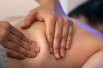Mains effectuant un massage sur le dos d'une patiente, geste précis illustrant les techniques manuelles en naturopathie
