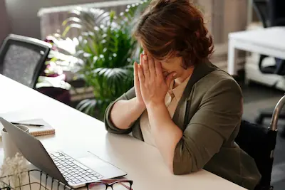 Femme épuisée au bureau, mains sur le visage devant son ordinateur, illustrant la fatigue chronique au quotidien