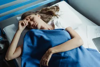 Femme allongée dans son lit en plein jour, épuisée, illustrant la fatigue persistante liée aux infections chroniques