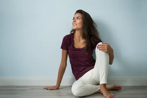 Femme assise au sol, dos appuyé contre un mur, regard calme et souriant, illustrant la sérénité émotionnelle