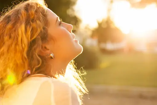 Femme au visage tourné vers la lumière dorée du soleil, illustrant les effets apaisants de la luminothérapie